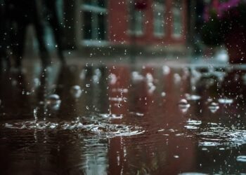 Close-up of raindrops splashing into a puddle, capturing reflections and textures in an outdoor urban setting.