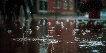 Close-up of raindrops splashing into a puddle, capturing reflections and textures in an outdoor urban setting.