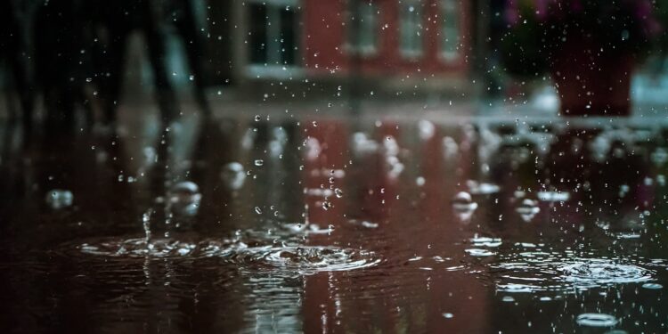Close-up of raindrops splashing into a puddle, capturing reflections and textures in an outdoor urban setting.